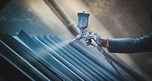 a person using a paint sprayer to paint metal products