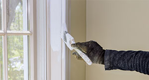 a person wearing dirty gloves to paint a window frame white
