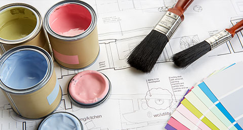 paint brushes, paint tins and a colour swatch on top of decorating plans