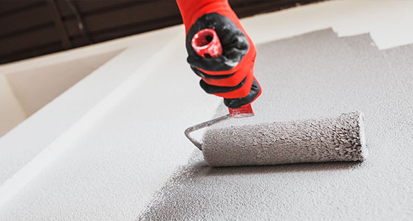 a person wearing a red and black glove using a paint roller to paint an exterior wall grey