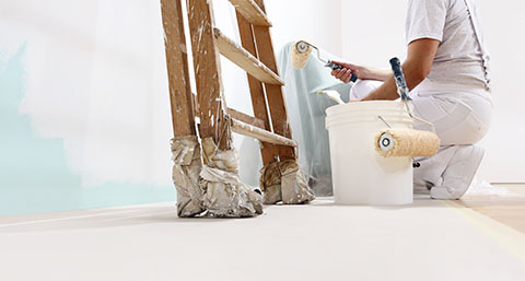 a person painting over a blue wall with a roller, with a wooden ladder to their left