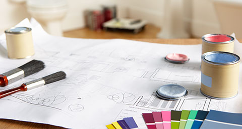 painting and decorating plans on a table, with paint pots, brushes and swatches on it