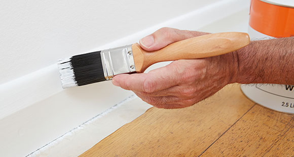 a person using a paintbrush to paint a skirting board white