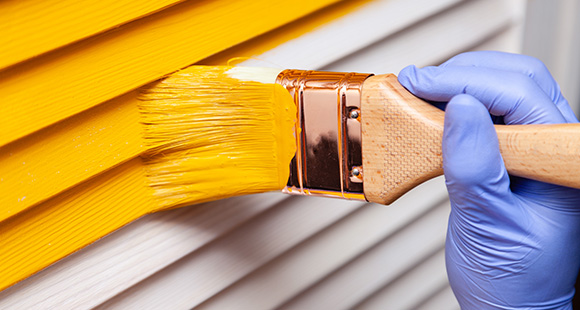 a person wearing a disposable glove using a paintbrush to paint an exterior yellow