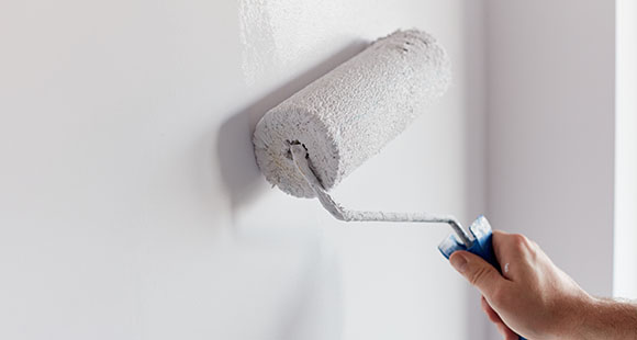 a person using a paint roller to paint a wall white