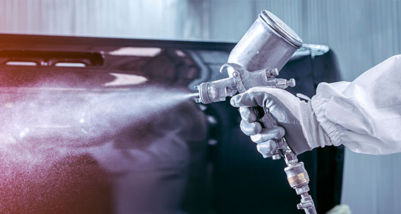 a man in protective wear using a spray painter to spray paint a metal part white
