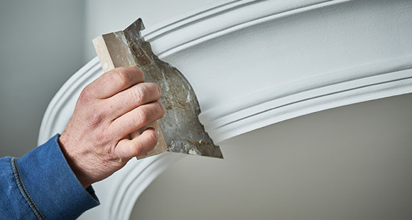 a person using a coving spatula to smooth the paint for a coving section of wall
