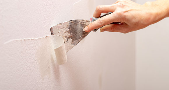 a person using a spatula to remove old white paint off of a wall
