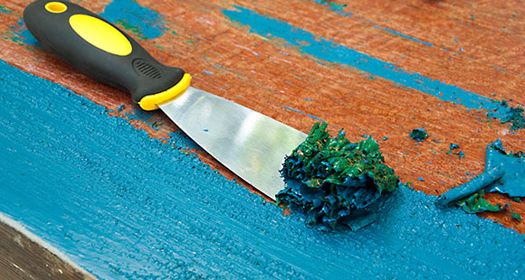 a spatula being used to scrape blue paint off of a wodden surface