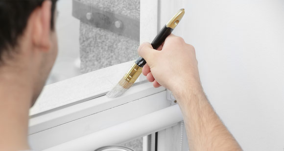 a man painting a small window sill white with a small paintbrush 