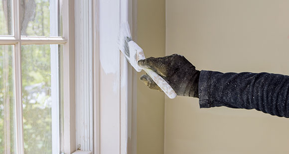 a gloved person painting a window bay white with a paintbrush